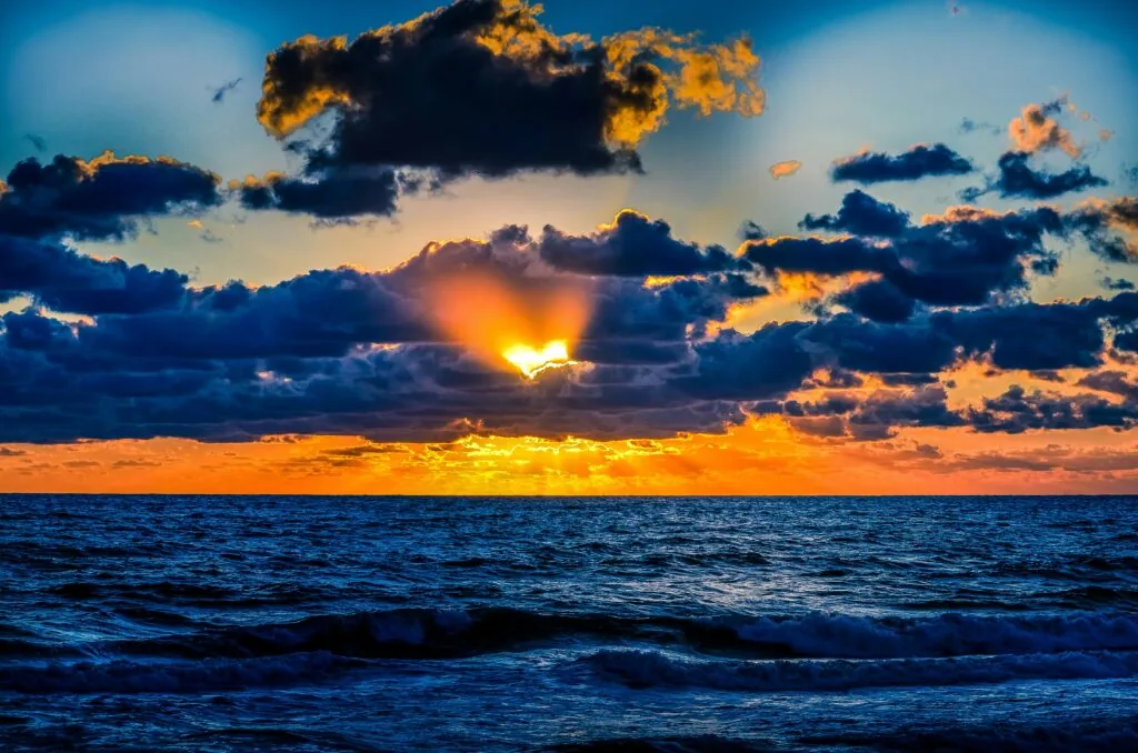 Sun setting over ocean with dramatic clouds in blue, orange, and gold tones