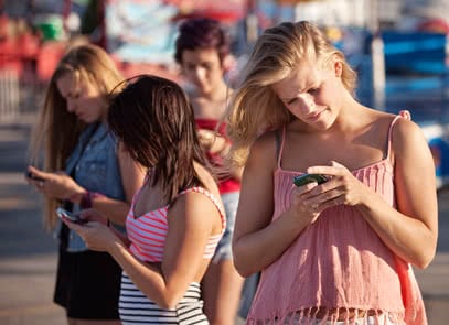 Four female teenagers using their phones outside