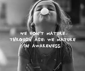 Black and white photo of a young child looking upward with text overlay reading 'We don't mature through age; we mature in awareness'