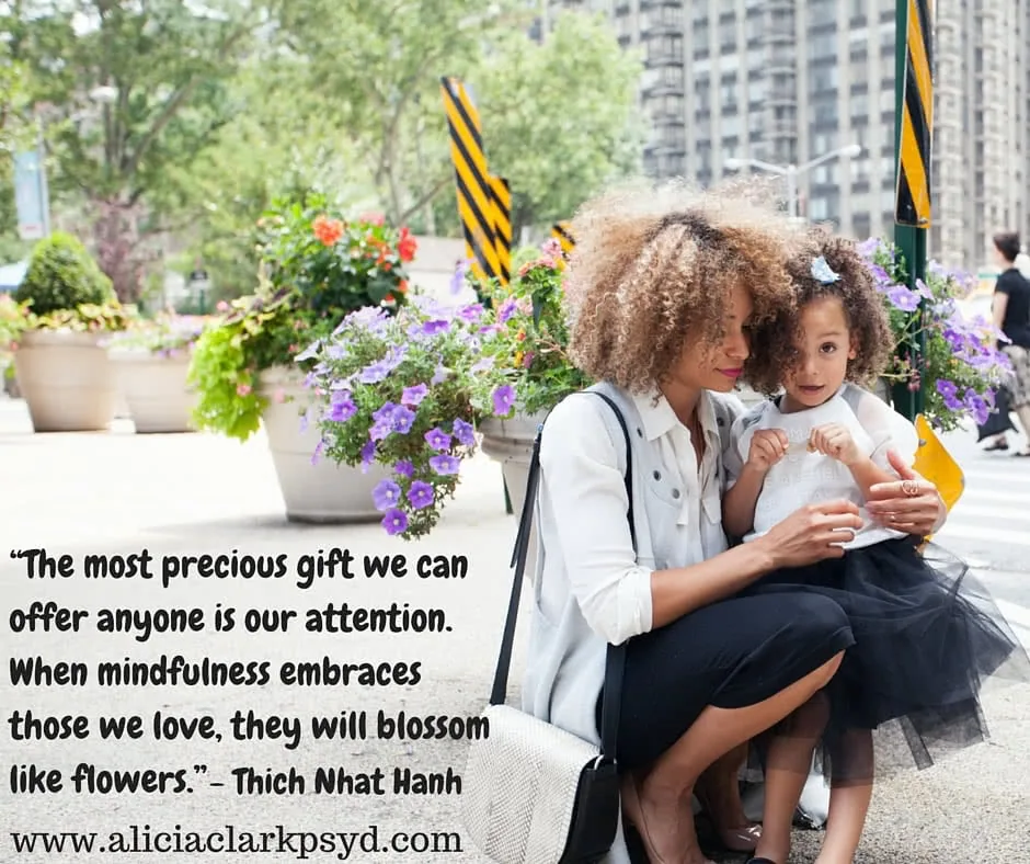 Adult and child sitting together outdoors among purple flowers with city buildings in background