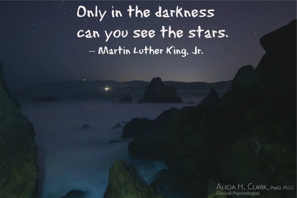 Dark rocky coastline at night with stars visible in sky above water, with quote text overlaid