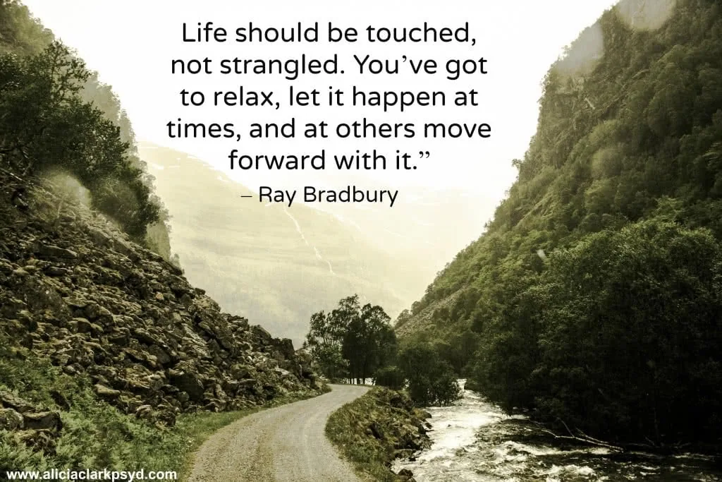 Mountain road with river flowing alongside, flanked by steep forested hillsides with inspirational quote about life by Ray Bradbury overlaid