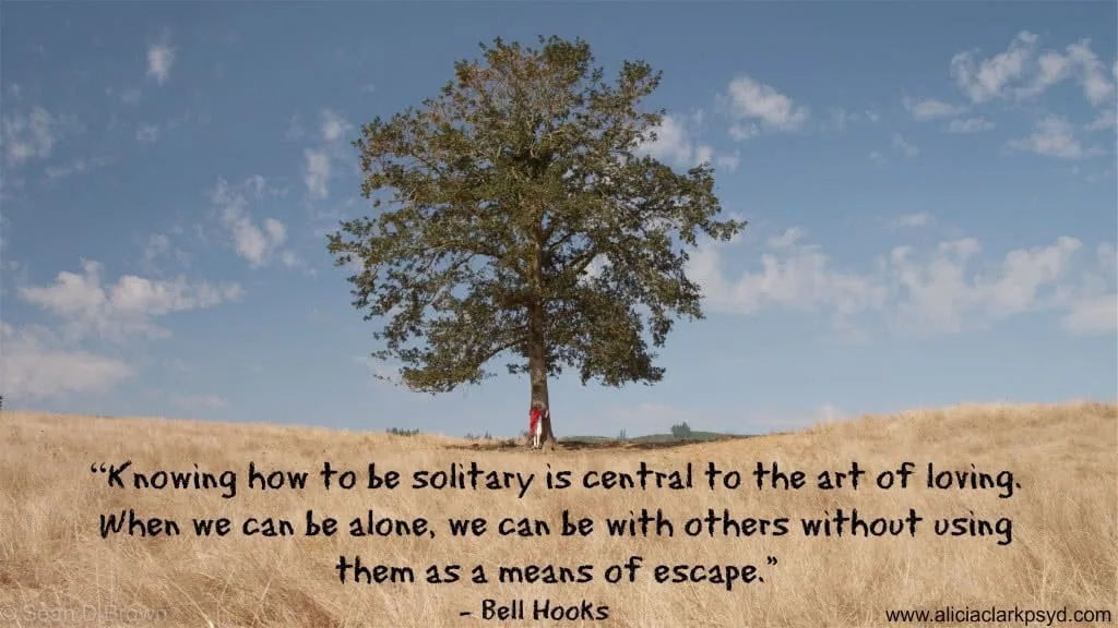 Person sitting alone beneath a solitary tree in an open field with blue sky and white clouds
