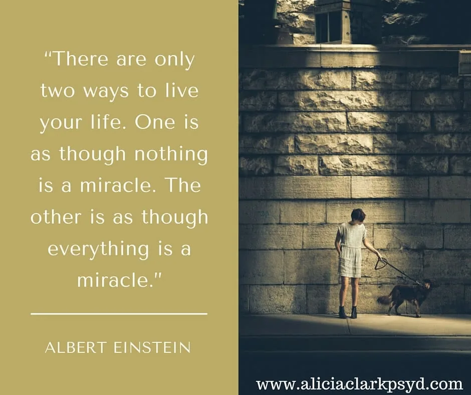 Child in light dress standing against stone wall with dog, with Albert Einstein quote about miracles on gold background