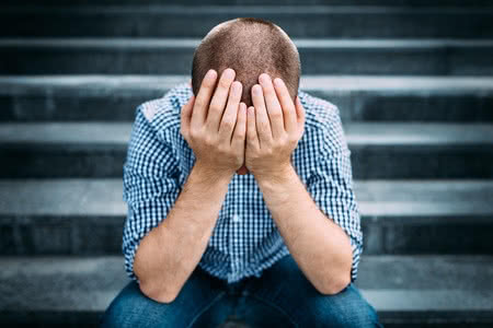 40346537 - outdoor portrait of sad young man covering his face with hands sitting on stairs. selective focus on hands. sadness, despair, tragedy concept
