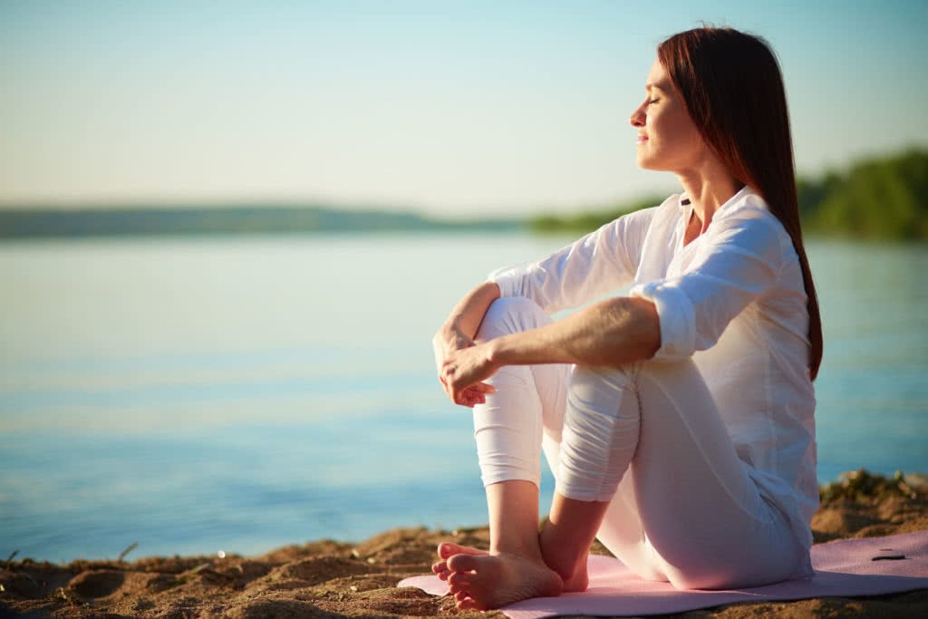 30050658 - side view of serene woman sitting on sandy beach against blue sky outdoors