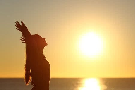 37323219 - woman breathing fresh air at sunset on the beach and raising arms