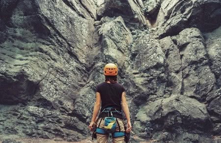 40985751 - young woman wearing in climbing equipment standing in front of a stone rock outdoor and preparing to climb, rear view