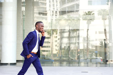 53356513 - side portrait of a happy young man in suit walking and talking on mobile phone