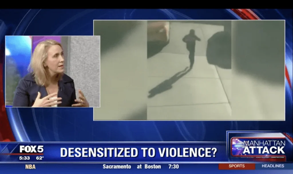 Woman in dark jacket speaking on FOX5 news broadcast discussing desensitization to violence, with security footage visible on screen.