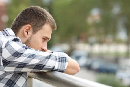 71228412 - side view portrait of a sad single man looking down from a balcony of a house  with an urban background