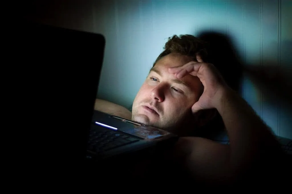 Man looking stressed while viewing laptop screen in dim lighting