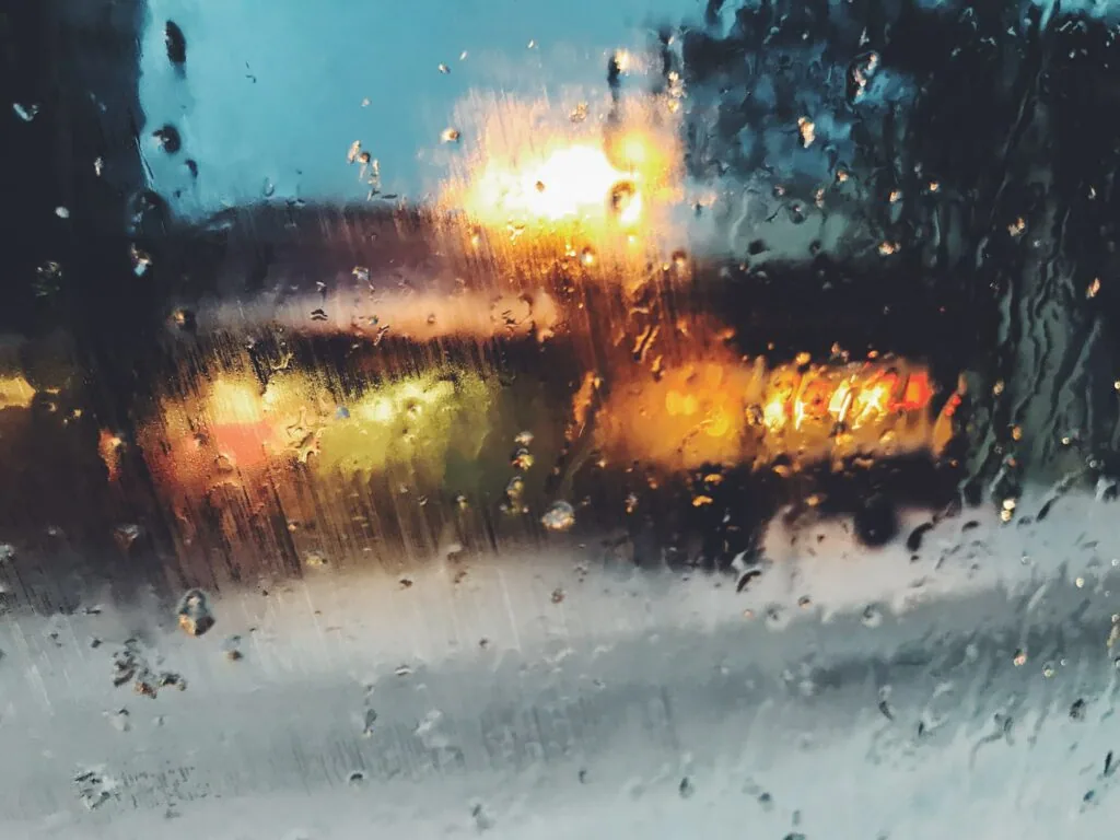 Wet windshield with raindrops and blurred city lights at dusk or dawn